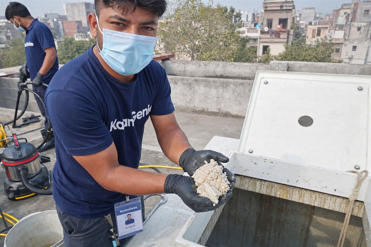 KaamGenie technician showing thick white chalky scale deposits scraped from inside a Delhi overhead water tank affected by hard water