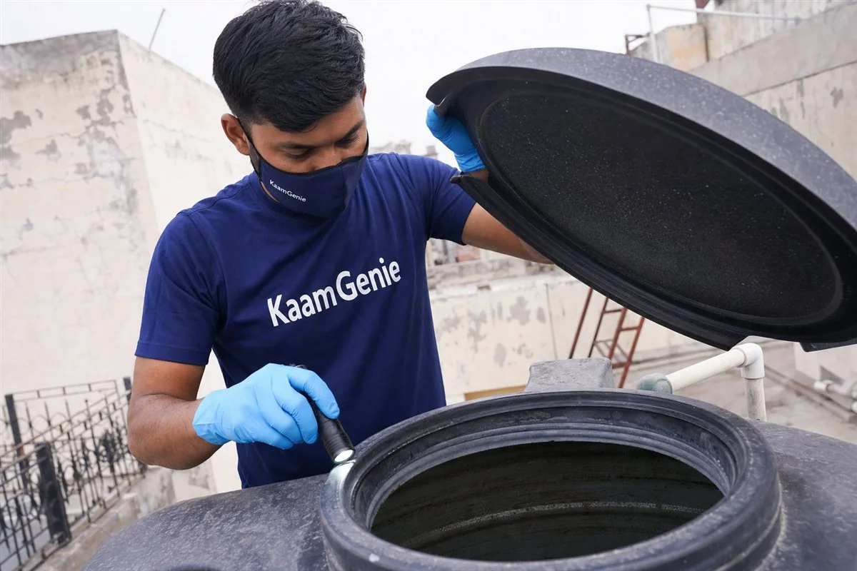 Close-up of a KaamGenie technician in navy uniform lifting the lid of a rooftop water tank to inspect for larvae in Delhi